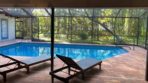 Piscina interna com duas espreguiçadeiras, cercada por um pátio de tijolos e grandes janelas que oferecem vista para um jardim exuberante.