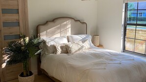 Quarto com cama de madeira, planta em vaso, luminária pendente e janela com vista para o exterior.