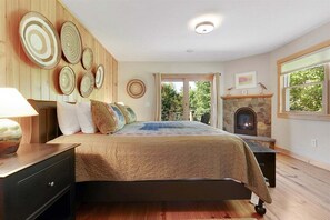 Ein Schlafzimmer mit Bett, Nachttisch, Lampe, Kamin und Blick ins Freie.