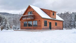 Puinen mökki, jossa on parveke, suuret ikkunat ja lumipeitteinen katto.
