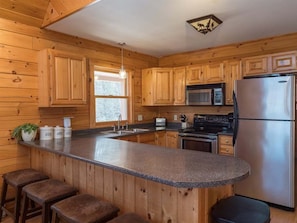 Una cocina con armarios de madera, encimera de granito, refrigerador de acero inoxidable y microondas.