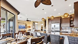 A modern kitchen with a large island, dining area with wicker chairs, and a ceiling fan. - Luxury Kapalua Golf Villa With Beautiful Sweeping Views (Lahaina)