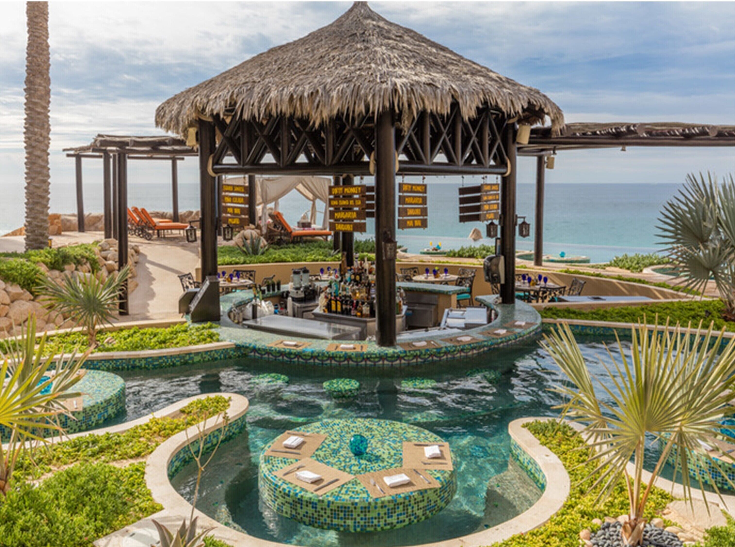 Un complexe hôtelier doté d’une piscine, d’un bar et d’une structure dont le toit est fait de chaume.