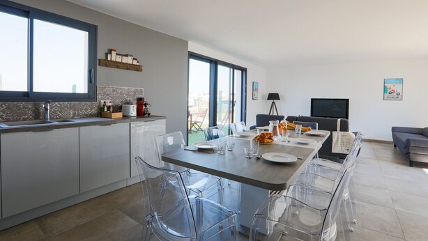 A modern kitchen with a dining area, large windows, and a flat-screen TV. - Equiped house for 4 adults and 4 children (Le Bois-Plage-en-Ré)