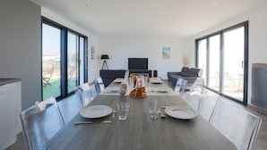 A modern dining area with a long table set for six, clear chairs, and a television in the background. - Equiped house for 4 adults and 4 children (Le Bois-Plage-en-Ré)