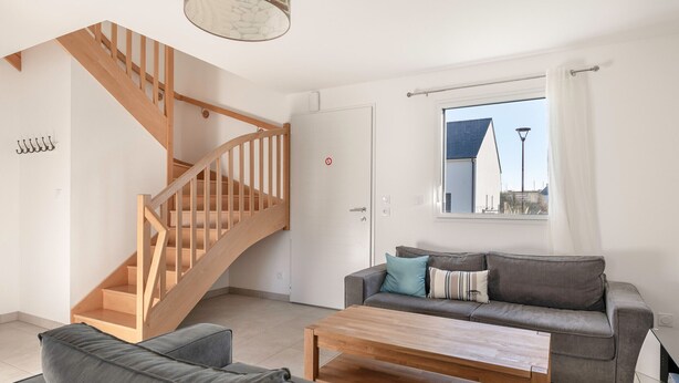 A modern living room with a wooden staircase, grey sofas, a wooden coffee table, and a large window with a view of buildings. - House for 4 adults / 4 children, fully equipped (Piriac-sur-Mer)