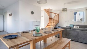 A modern dining area with a wooden table set for four, a staircase, and a grey sofa in the background. - House for 4 adults / 4 children, fully equipped (Piriac-sur-Mer)