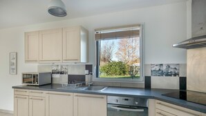 A modern kitchen with light wood cabinets, a stainless steel sink, a built-in microwave, and a window with a view of greenery. - House for 4 adults / 4 children, fully equipped (Piriac-sur-Mer)