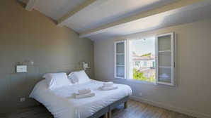 A bedroom with a bed, a nightstand, a lamp, and a window with a view of buildings outside. - Sunny appartment for 6 people (Le Bois-Plage-en-Ré)