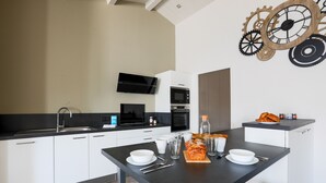 A modern kitchen with white cabinets, a black countertop, and a dining table set with plates, glasses, and a loaf of bread. - Sunny appartment for 6 people (Le Bois-Plage-en-Ré)