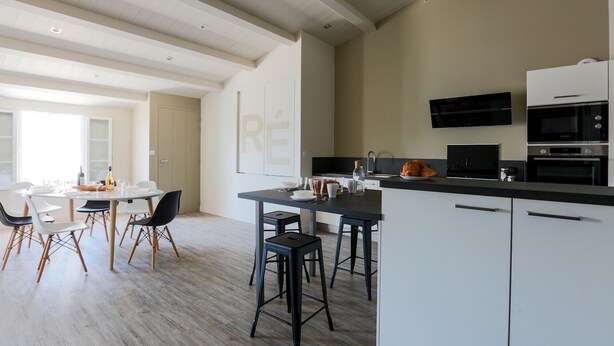 A modern kitchen with white cabinets, black countertops, and a central island with stools. - Sunny appartment for 6 people (Le Bois-Plage-en-Ré)