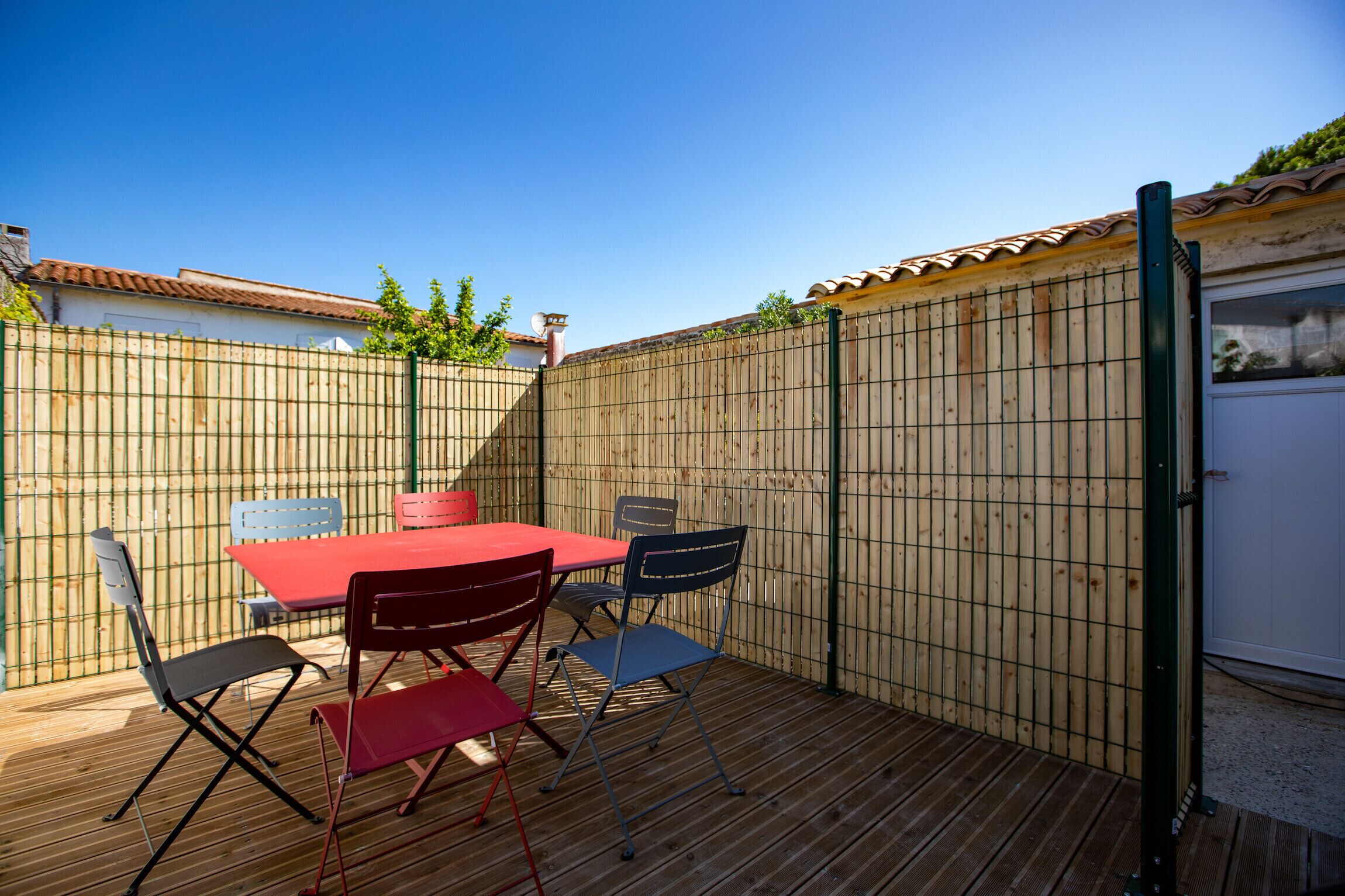 A wooden deck with a red table and four chairs.