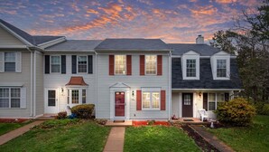 A two-story residential building with a front porch, a small garden, and a clear sky. - GannonHeights: Work-Friendly & 40 mins to DC (Sterling)