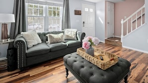 A living room with a grey sofa, a black ottoman, and a wicker basket with flowers. - GannonHeights: Work-Friendly & 40 mins to DC (Sterling)