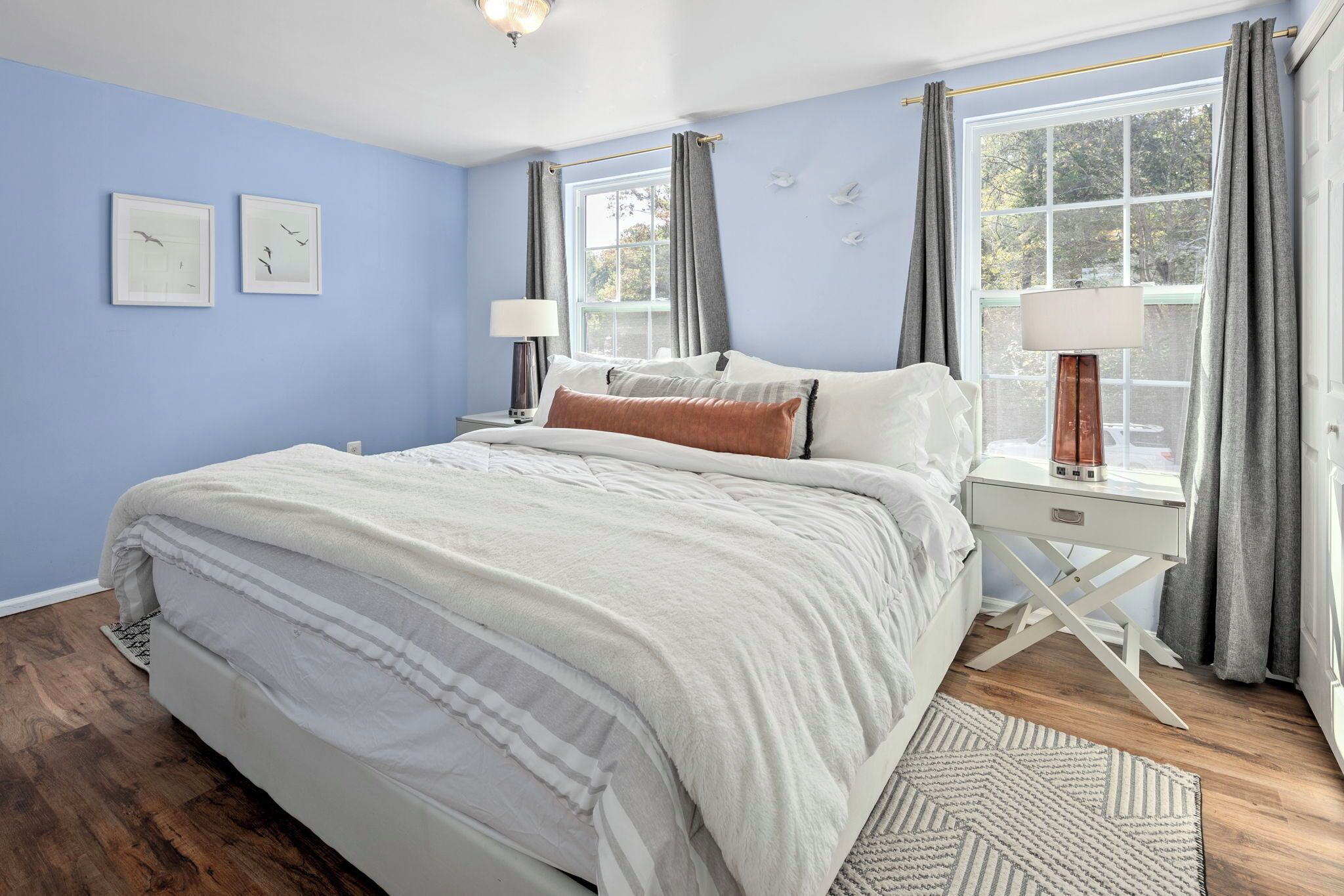 Une chambre à coucher avec un grand lit, deux tables de chevet, une fenêtre avec des rideaux et un mur orné de tableaux.