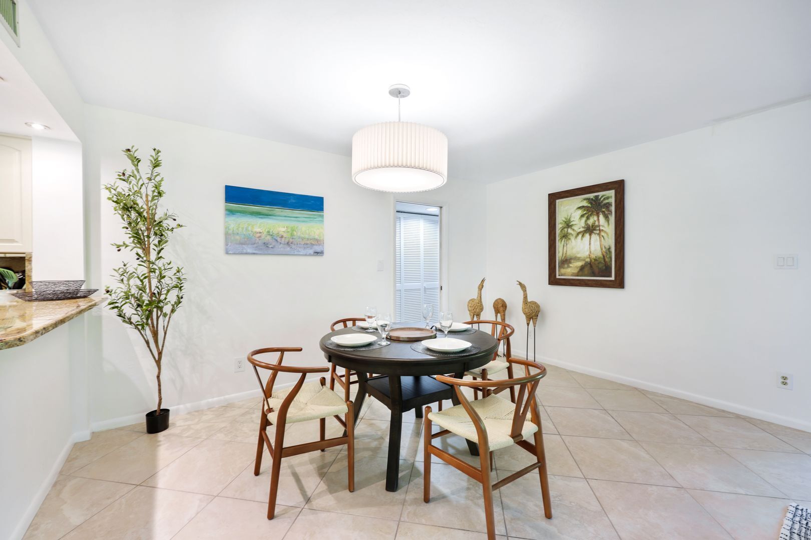 A dining area with a round table, chairs, a potted plant, and artwork on the walls.