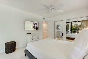 Un dormitorio con una cama, ventilador de techo, televisor, cómoda y puerta corrediza que da a un balcón.