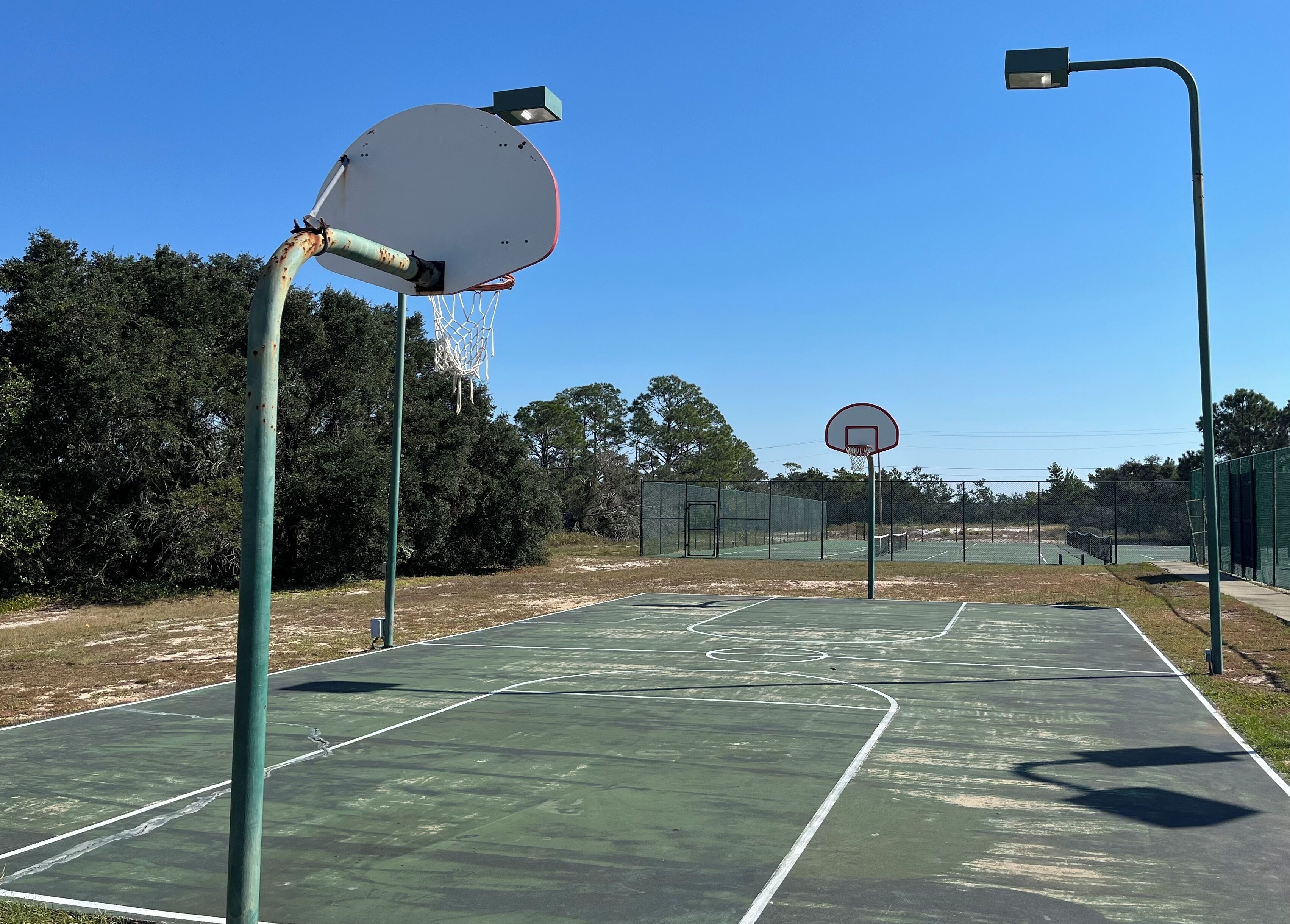 Ein Basketballplatz im Freien mit zwei Körben, umgeben von einem Zaun und Bäumen.