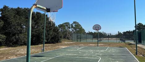 Ein Basketballplatz im Freien mit zwei Körben, umgeben von einem Zaun und Bäumen.