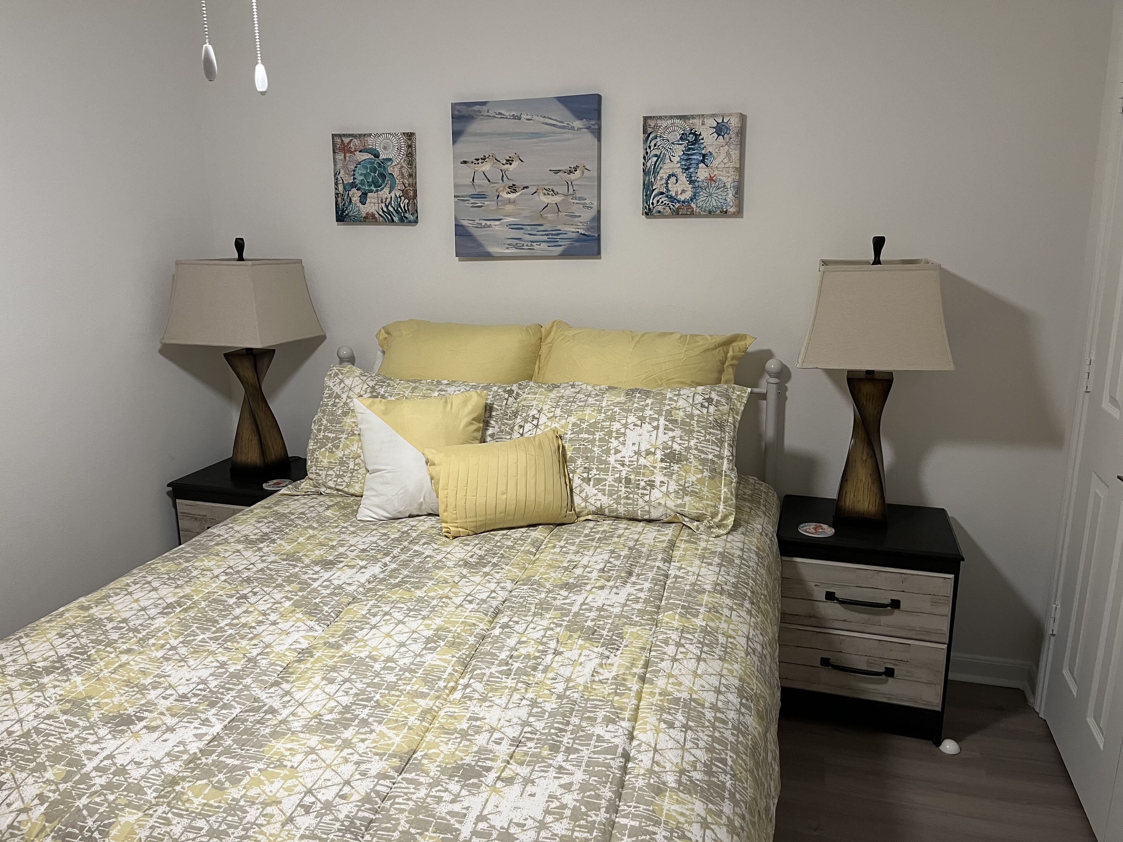 A neatly made bed with patterned bedding, two bedside tables with lamps, and three wall art pieces.