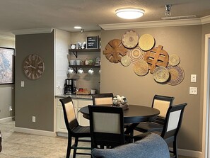 A dining area with a round table and chairs, a clock on the wall, and decorative plates.