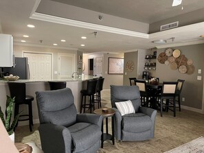 A modern kitchen with a central island, dining area with chairs, and a living room with sofas.