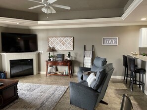 A living room with a fireplace, a television, a sofa, a coffee table, and a bar area.