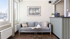 Un espace d’accueil moderne avec un canapé gris, deux tables rondes, une œuvre d’art encadrée, un comptoir d’accueil et une vue dégagée grâce à de grandes fenêtres.