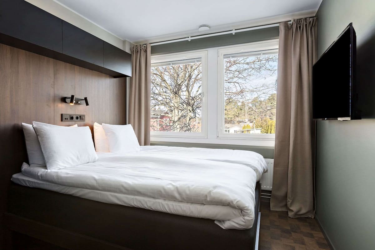 Une chambre d’hôtel moderne avec un grand lit, un téléviseur à écran plat et une fenêtre avec des rideaux.