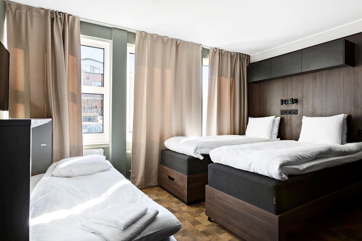 Une chambre d’hôtel avec deux lits, une armoire et une fenêtre avec des rideaux.