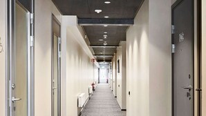 Un long couloir étroit, avec des portes de chaque côté, un sol recouvert de moquette et des spots encastrés au plafond.