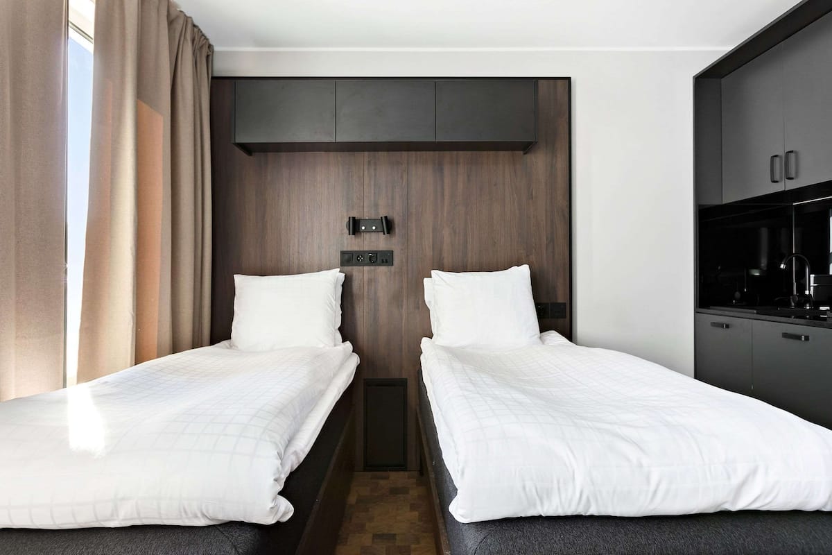 Une chambre d’hôtel avec deux lits simples, un mur décoratif en bois, une armoire intégrée et une kitchenette.