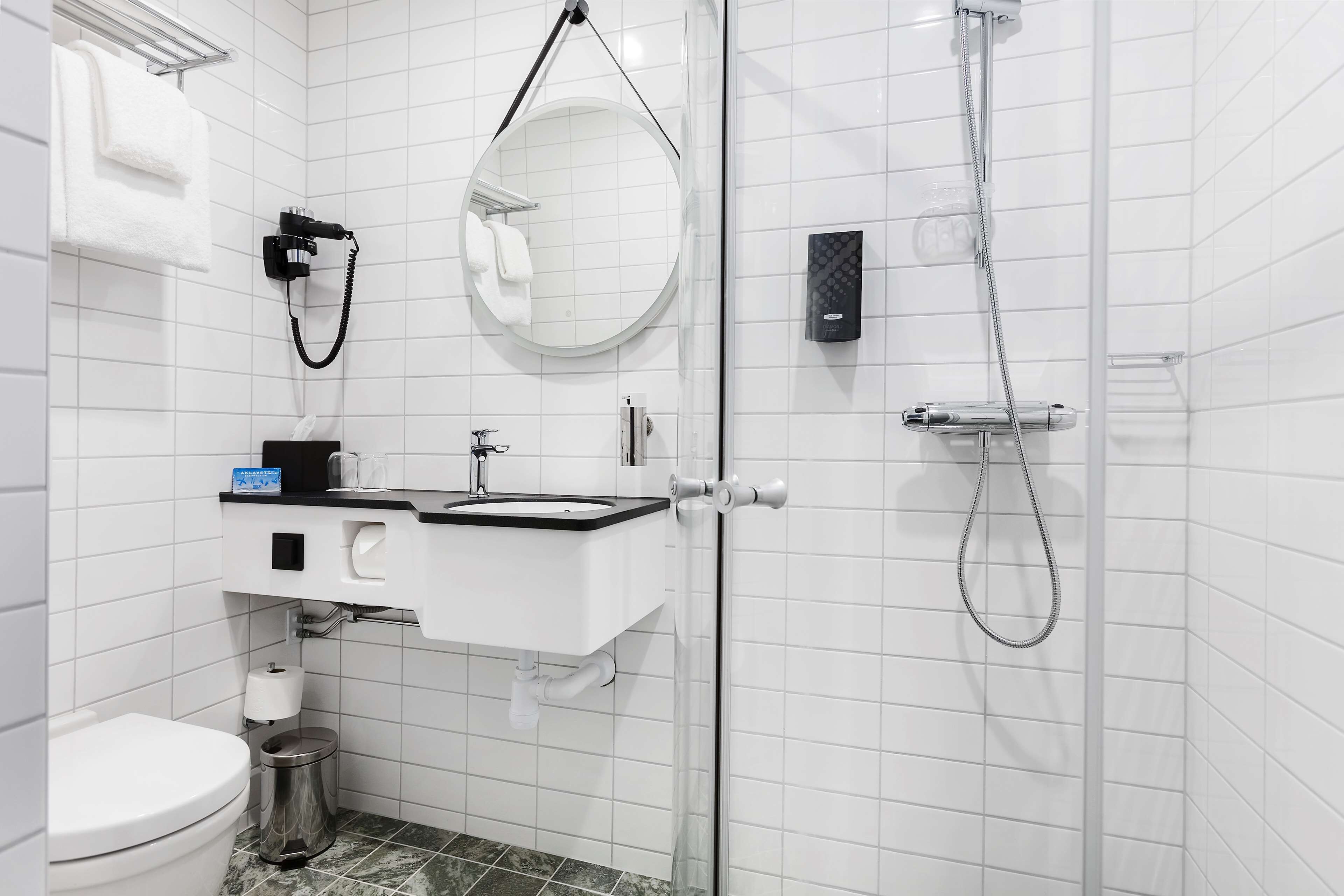 Un baño moderno con inodoro, lavabo, espejo, toallero y ducha.