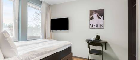 A bedroom with a bed, a TV mounted on the wall, a small desk with a chair, and a poster on the wall.