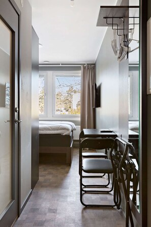 A compact room with a bed, a desk, and a chair, a window with curtains, and a television on the wall. - Sure Hotel Studio by Best Western Bromma (Bromma)