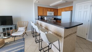 A modern kitchen with a bar area, wooden cabinets, and a flat-screen TV. - Inn at Dauphin Island 306 Efficient 1BR sleeps 6 with Beautiful Views!! (Dauphin Island)