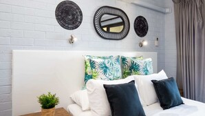 Ein ordentlich eingerichtetes Schlafzimmer mit einem weißen Kopfstück, einem Bett mit weißen und dunkelblauen Kissen, einem Nachttisch mit einer Pflanze und drei an der Wand befestigten Spiegeln.
