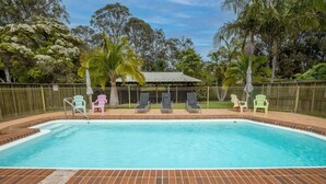 A rectangular pool with a brick border, surrounded by a fence. There are lounge chairs and a covered seating area with a roof. - Seafront Getaway Studio, Great Location with Pool (Batemans Bay)