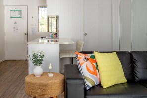 A modern living room with a black leather sofa, a round wicker ottoman, and a small white vase with a plant. - Seafront Getaway Studio, Great Location with Pool (Batemans Bay)