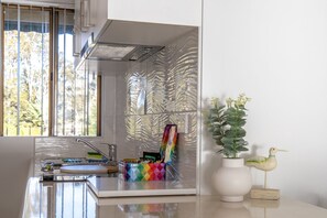 A modern kitchen with a built-in stove, a sink, and a window with a view of trees. - Seafront Getaway Studio, Great Location with Pool (Batemans Bay)
