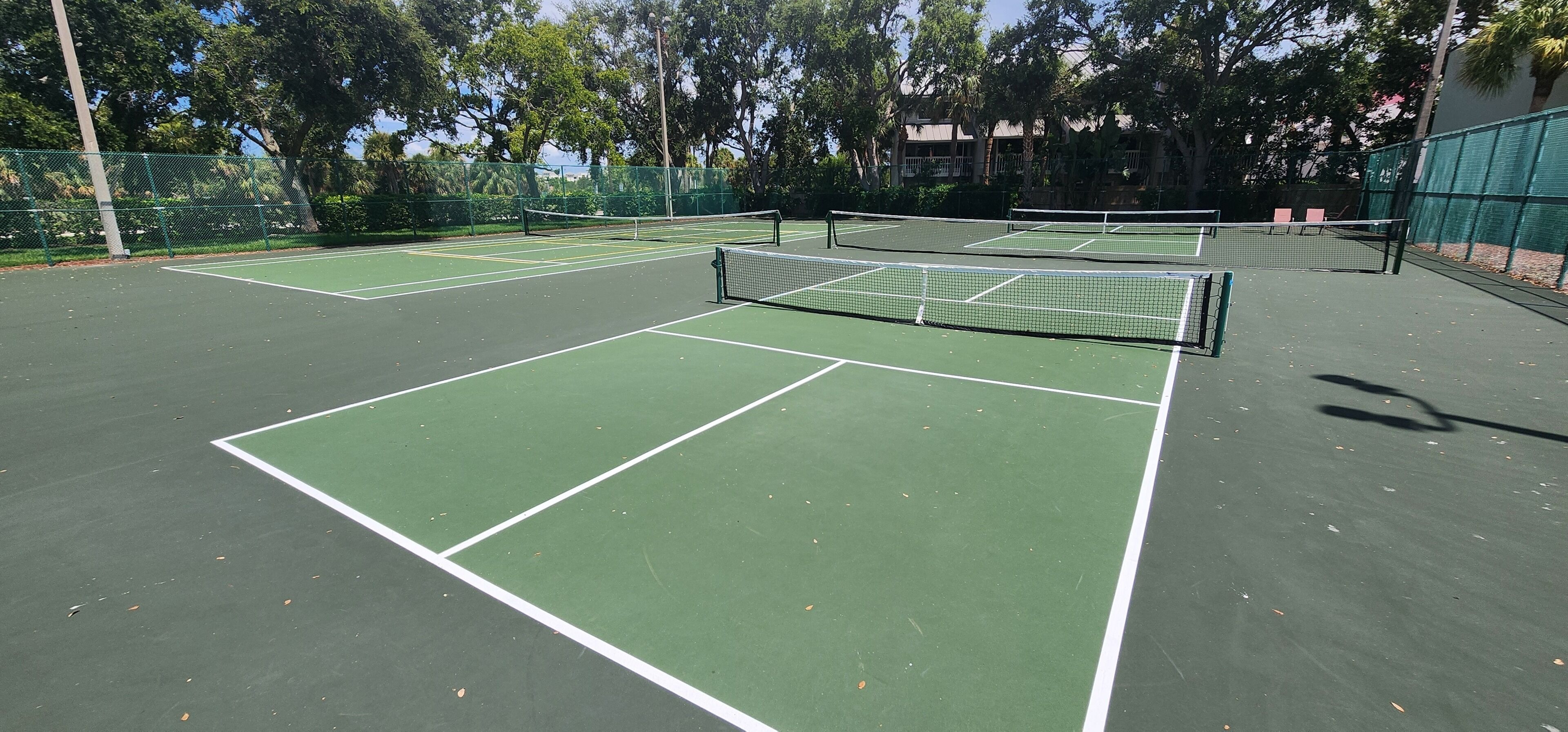 A tennis court with multiple courts, surrounded by trees and a fence.