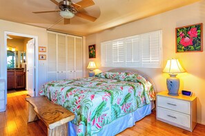 A bedroom with a bed, bedside lamps, a nightstand, a wooden bench, a ceiling fan, and a window with shutters.