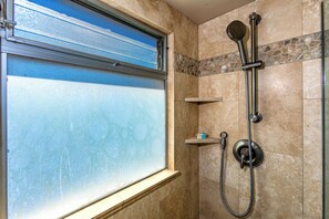 A shower with a handheld showerhead and a wall-mounted faucet, a window with frosted glass, and a stone-tiled shower area.