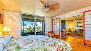 Une chambre d’hôtel avec un lit, un ventilateur de plafond, une porte-fenêtre coulissante donnant sur un balcon et une vue sur des palmiers.
