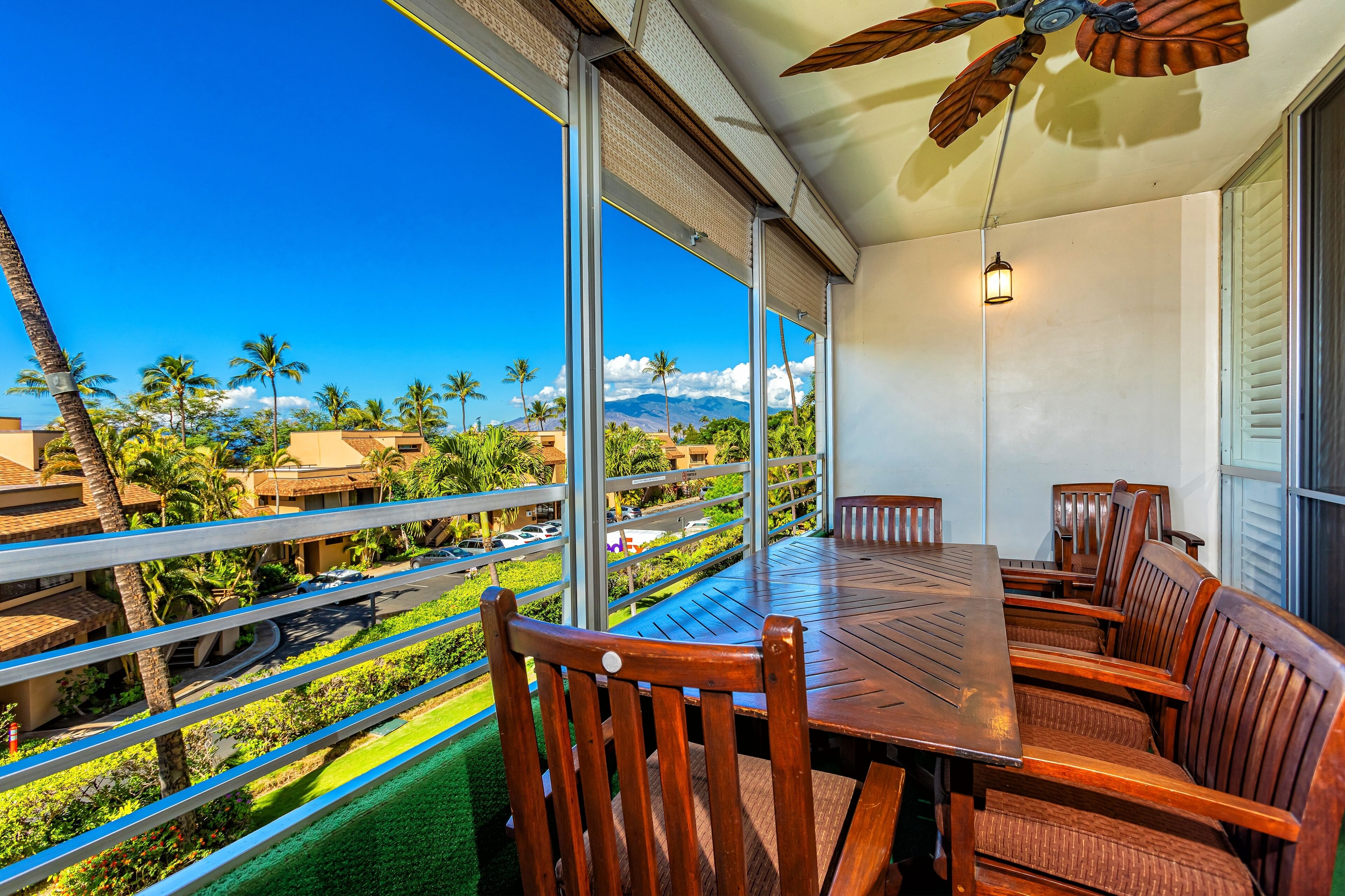 A balcony with a wooden table and chairs, large windows offering a view of palm trees and mountains.