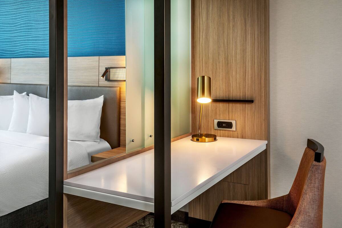 Una habitación de hotel con cama, mesita de noche, una silla y una lámpara en la pared.