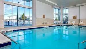 Une piscine intérieure à l’eau d’un bleu cristallin, dotée de grandes fenêtres et de chaises longues blanches.