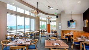 Un restaurant avec des tables et des chaises, de grandes fenêtres et une vue sur la mer.