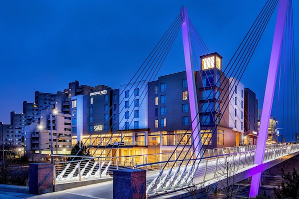 Un puente moderno con cables iluminados, un hotel de varios pisos y una vista despejada del área urbana circundante.