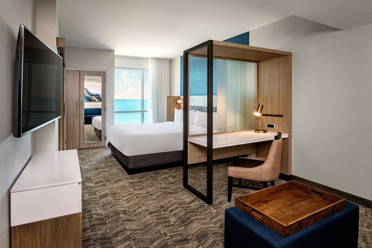 Habitación de hotel con cama, escritorio, silla, televisión y vista al océano.